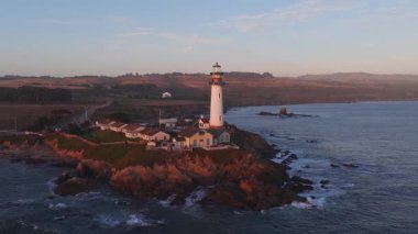 Günbatımında Kaliforniya 'daki Pigeon Point Deniz Feneri' nin hava manzarası kayalara, açık arazilere çarpan dalgalar ve manzaradaki dolambaçlı bir yol..