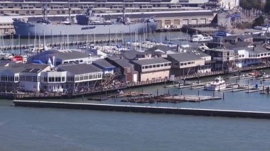 San Francisco 'nun 39. rıhtım bölgesinin havadan görünüşü rıhtımlı tekneler, rıhtıma bakan binalar, bir donanma gemisi ve marina üzerinde yavaş çekim hareketi..