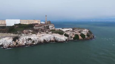 Cezaevi, deniz feneri, engebeli arazi ve sakin körfez sularıyla Alcatraz Adası 'nın pürüzsüz hava manzarası. Ufukta şehrin ufku görünüyor..
