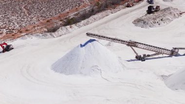 Nevada 'daki bir tuz madenciliği tesisi, tuz yığınlarına tuz taşıyan bir taşıyıcı bandı gösteriyor. Kamyonlar ve makineler seyrek bitki örtüsüyle çölde çalışır..