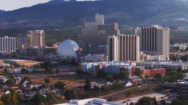 Reno, Nevada 'nın hava görüntüsü, gün batımında dönüm hareketiyle. Önemli noktalar arasında Gümüş Miras Kubbesi, yüksek binalar ve uzak dağlar yer alıyor..