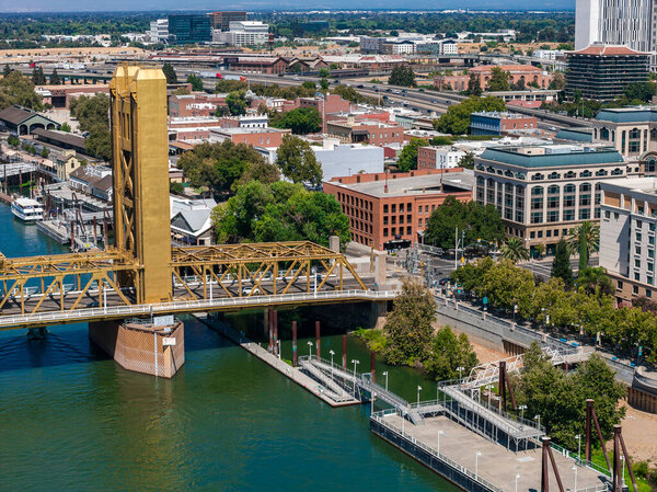 Вид с воздуха на Сакраменто, Калифорния, с золотым мостом через реку Сакраменто, окруженный историческими и современными зданиями и зеленью.