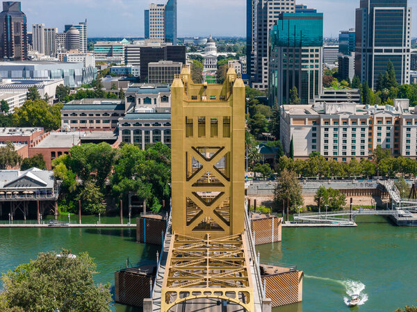 Вид с воздуха на Сакраменто, Калифорния, с золотым Тауэрским мостом, зданием Капитолия штата, городским горизонтом, зеленью на берегу реки и лодкой на реке.