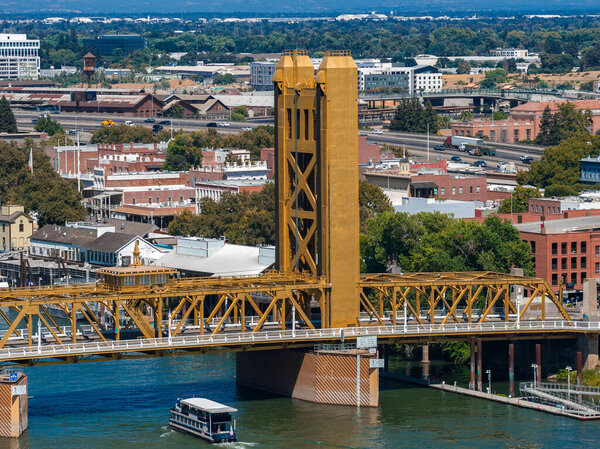 Мост Золотая башня охватывает реку Сакраменто с лодкой ниже, в окружении исторических зданий, деревьев вдоль улиц, и городской архитектуры.
