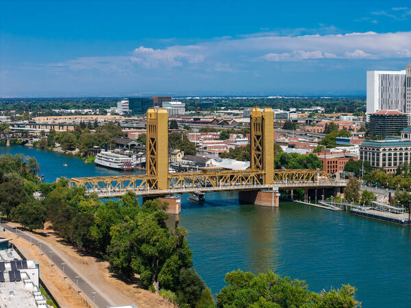 Вид с воздуха на Сакраменто, Калифорния, с золотым мостом через реку Сакраменто, окруженный зеленью и городской архитектурой.