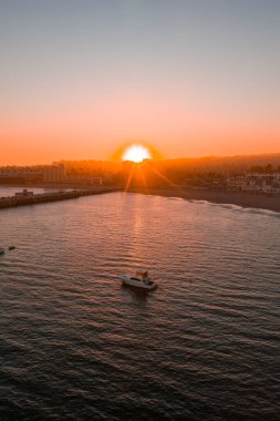 Sıcak turuncu bir günbatımı, Santa Cruz sahil şeridini, rıhtımı, sakin okyanusu ve Kaliforniya 'da binalar ve palmiye ağaçlarıyla aydınlatır..