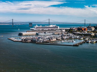 San Francisco rıhtımı, rıhtıma yanaşmış bir yolcu gemisi, balıkçı iskelesi binaları, rıhtımlar, küçük tekneler ve sakin mavi sulara sahiptir..