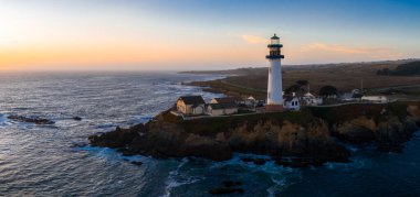 Kaliforniya 'da kıyı uçurumundaki Pigeon Point Deniz Feneri' nin hava manzarası. Etrafı okyanus dalgaları, engebeli kıyı şeridi ve ılık günbatımı renkleriyle çevrili..