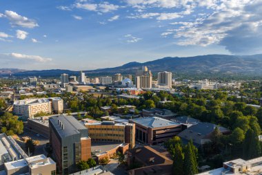 Reno, Nevada şehir merkezinde, Sierra Nevada dağlarına karşı kurulu yüksek binalar ve kumarhaneler var, yeşil ve açık mavi gökyüzü.