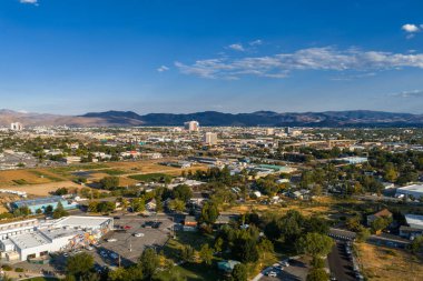 Aerial view of Reno, Nevada, showcasing downtown casinos, residential areas, and the Sierra Nevada mountains under a sunny sky with scattered clouds.