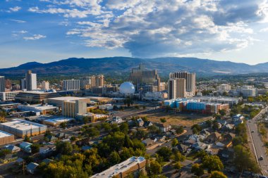 Reno, Nevada 'nın havadan görünüşü, şehir merkezindeki yüksek binalar, Gümüş Miras' ın beyaz kubbesi, ağaçlarla kaplı yerleşim yerleri, ve dağ zeminleri..