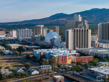 Reno, Nevada şehir merkezinin havadan görünüşü, arka planda Silver Legacy Kumarhanesinin gümüş kubbesini, modern binaları ve Sierra Nevada dağlarını gösteriyor..
