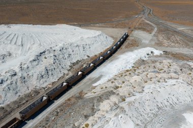 Aerial view of a Nevada salt mining site with white salt mounds, a freight train, dirt roads, sparse vegetation, and intersecting tracks.