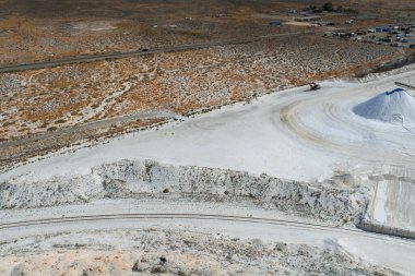 Aerial view of a salt mining site in Nevada featuring white salt mounds, a red industrial vehicle, dirt roads, railway tracks, and nearby facilities.