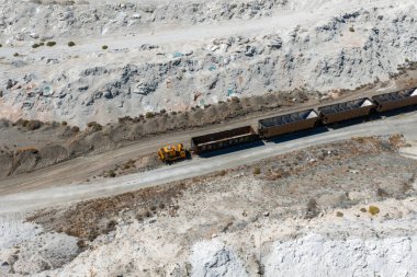 Aerial image of a salt mining site in Nevada featuring rugged terrain, a yellow vehicle pulling freight cars, sparse vegetation, and rocky outcrops.