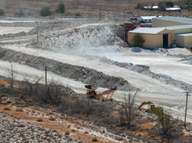 Nevada 'da beyaz tuz tepeciklerini, endüstriyel ekipmanları, bej bir binayı, toprak yolları ve kurak araziyi gösteren bir tuz madenciliğinin hava görüntüsü..