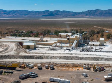Nevada 'da bej binalar, makineler ve beyaz tuz yığınları olan bir tuz madenciliğinin havadan görünüşü bir çöl ve dağ zeminine karşı kuruludur..