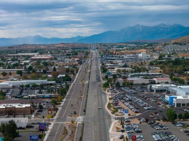Carson City, Nevada 'daki düz bir yolun havadan görünüşü. Ticari binalar, otoparklar ve ağaçlarla çevrili. Bulutlu bir gökyüzünün altında dağlar..