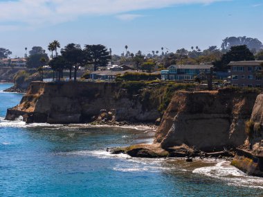 Capitola, California kıyı manzarası, uçurumlar, renkli evler, palmiye ağaçları ve okyanus dalgaları dağınık mavi bulutların altında.