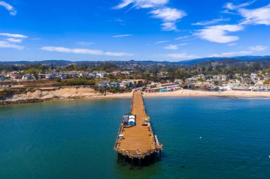 Pasifik Okyanusu üzerinde ahşap bir iskeleye sahip Capitola, Kaliforniya 'nın hava manzarası, renkli sahil binaları, kumlu kıyılar, ve kayan tepeler.