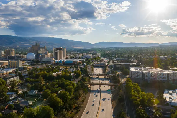 Reno, Nevada 'nın havadan görünüşü, şehir merkezindeki kumarhaneler, yüksek binalar, kubbe şeklinde bir yapı, otoyollar ve bulutlu bir gökyüzünün altındaki dağ manzarası..