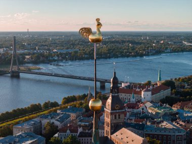 Riga, Letonya 'nın hava manzarasında altın horoz rüzgar gülü, Riga Katedrali, Daugava Nehri, Vansu Köprüsü ve Ulusal Kütüphane yer alıyor..