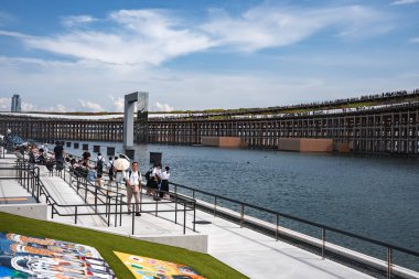 Osaka 'da 2025 Dünya Fuarı' nda bir rıhtım bölgesi yeşillik, yansıtıcı heykel, patikalar ve renkli afişler gibi yapılara sahiptir..