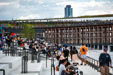 Ziyaretçiler, bir rıhtım kenarındaki katmanlı beton koltukları, yapıya benzer ahşap bir ızgarayı ve Japonya 'nın Osaka kentindeki yeşil bir çatı geçidini keşfediyorlar..