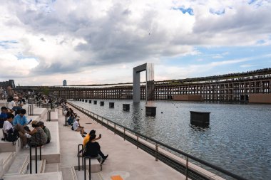 Japonya 'nın Osaka kentindeki bulutlu bir gökyüzünün altında, ziyaretçiler ve yükseltilmiş bir yürüyüş yolu ile, sakin bir oturağın yanındaki sulardan metalik bir yapı yükselir..