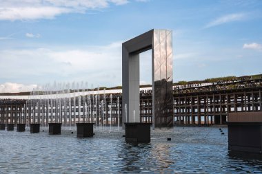 Japonya 'nın Osaka kentindeki yeşil çatılı ve açık mavi gökyüzüne karşı senkronize fıskiyelerle donatılmış su havuzu üzerinde yansıtıcı metalik bir kemer..