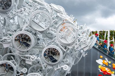 Dünya Fuarı 2025, Osaka 'da dairesel elementleri ve aynaları olan gelecekçi beyaz yapı. Kırmızı şapkalı ve renkli duvar tasarımlı insanlar görülebilir..