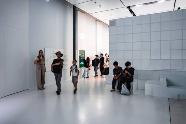 Beyaz duvarları, şebeke tasarımı, yürüyen ya da banklarda oturan ziyaretçiler ve sergi ortamında bilgilendirme amaçlı görüntülerle minimalist iç mekan.