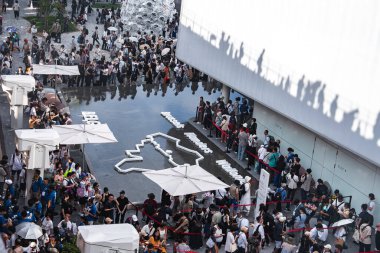 Ziyaretçiler harita tasarımı, modern beyaz bir bina ve Japonya 'daki Dünya Fuarı 2025' teki heykel gibi metalik bir ağaç ile yansıtıcı bir su özelliğini keşfediyorlar..