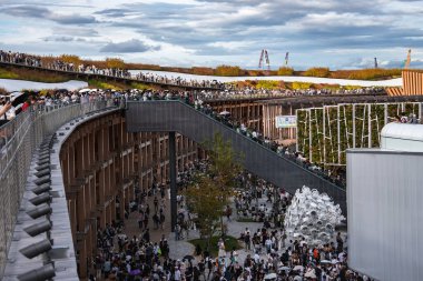 Ziyaretçiler, devam etmekte olan inşaat çalışmaları sırasında kıvrımlı bir yürüyüş yolu, dikey bahçe duvarı ve metal baloncuk heykeli olan çok katlı bir açık alanda toplanıyorlar..