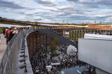 Ziyaretçiler, Japonya 'nın Osaka kentinde 2025 Dünya Fuarı' ndaki çok katlı bir açık hava mekanını kıvrımlı bir bina, metal heykel ve yükseltilmiş yollarla dolduruyorlar..