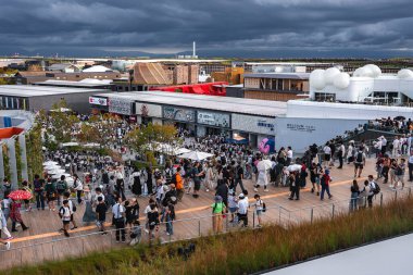 Ziyaretçiler, Osaka 'daki Dünya Fuarı 2025' te yeşilliklerle çevrili ahşap bir gezinti alanı boyunca yürüyorlar. Pavilionlar, eşsiz mimari ve kıyı manzaraları görülebilir..