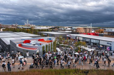 Ziyaretçiler, Sırbistan da dahil olmak üzere çağdaş pavyonlarla çevrili Osaka 'daki 2025 Dünya Fuarı' nda, bulutlu bir tepe arkaplanı ile ahşap bir patika yolda yürüyorlar..