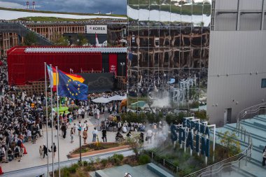 Ziyaretçiler, Japonya 'nın Osaka kentinde düzenlenen 2025 Dünya Fuarı' nda İspanya Köşkü 'nü ve koyu kırmızı Kore Pavyonu' nu keşfediyorlar. Bayraklar görünür..