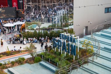 Dünya Fuarı 2025 'teki İspanya Pavyonu' nda modern mimari, peyzaj yeşili ve ziyaretçilerin yakınlarda toplandığı yansıtıcı cepheler yer alıyor..