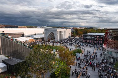 Ziyaretçiler, Japonya 'nın Osaka kentinde 2025 Dünya Fuarı' nı keşfederek, kemerli girişi, manzaralı yeşilliği ve yükseltilmiş bir yürüyüş yolu bulunan modern bir pavyona sahipler..