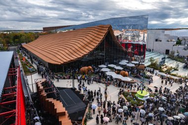 Ziyaretçiler, Japonya 'nın Osaka kentindeki 2025 Dünya Fuarı' nda yansıtıcı cam, açık hava koltukları ve heykelleri olan dalgalı bir teras çatısı yakınında toplandılar..