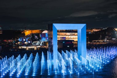 Japonya, Osaka 'da 2025 Dünya Fuarı' nda canlı bir gece sahnesi. Çeşmelerin, modern çadırların ve gösterinin keyfini çıkaran kalabalıkların olduğu parlak bir kemer..