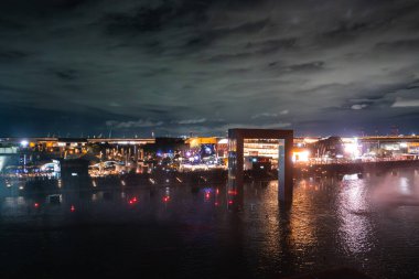 Japonya, Osaka 'da 2025 Dünya Fuarı' nda canlı bir gece sahnesi, parlayan pavyonlar, aydınlık dikdörtgen bir yapı ve bir su kütlesi üzerinde yansımalar..