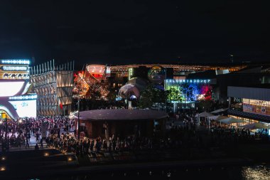 Modern mimari, renkli ışıklar ve Kolombiya pavyonunun bayrak renkleriyle aydınlatıldığı Osaka, Japonya 'daki 2025 Dünya Fuarı' nda canlı bir gece sahnesi..