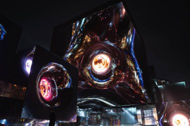 Yansıtıcı metalik yüzeyleri, parlayan dairesel tasarımları ve Japonya 'nın Osaka kentindeki parlak turuncu ve mavi ışıklandırması olan fütüristik bir yapının gece görüntüsü..