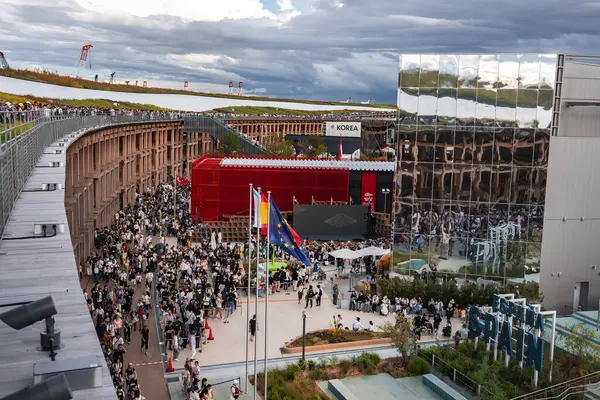 Dünya Fuarı 2025 'te, modern yapılar, ulusal bayraklar ve yeşil alanlarla çevrili, parçalı bulutlu gökyüzü altında, Japonya' nın Osaka şehrinde, ziyaretçiler toplandı..