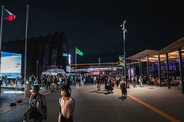 Japonya, Osaka 'da 2025 Dünya Fuarı' nın canlı bir gece görüntüsü aydınlık yollar, modern pavyonlar, ulusal bayraklar ve büyük bir dijital ekran boyunca kalabalıkları gösteriyor..