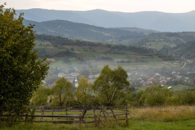 Etrafı görkemli dağlarla çevrili sakin bir çayırda dişi bir sanatçı tuvalindeki doğal güzelliği yakalamaya odaklanıyor. Sabah ışığı, o çalışırken sakin atmosferi güçlendirir..