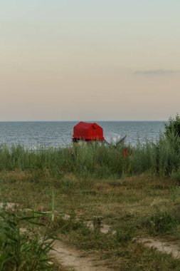 Canlı kır çiçekleri Karadeniz kıyısındaki çimenli araziyi işaretleyerek, öğleden sonranın rahatlatıcı atmosferini yakalıyor. Çarpıcı kırmızı bir yapı ufukta huzur içinde duruyor..