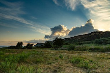 Karadeniz kıyısında, güneş batmaya başladığında kır çiçekleri rüzgarda hafifçe sallanıyor. Görkemli bulutlar gökyüzünü boyarken doğa uyum ve sükunet içinde gelişiyor..